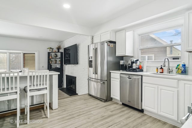 kitchen with sink, light hardwood / wood-style flooring, appliances with stainless steel finishes, white cabinets, and a brick fireplace