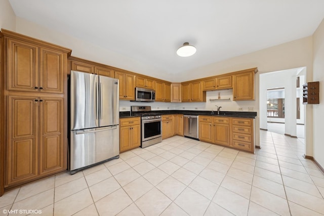 kitchen featuring appliances with stainless steel finishes, dark stone countertops, sink, and light tile patterned floors