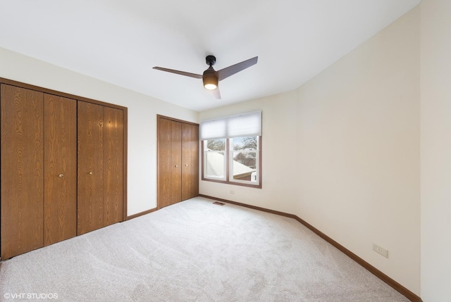 unfurnished bedroom featuring two closets, ceiling fan, and light carpet