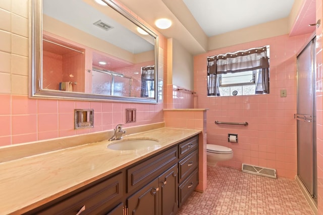 bathroom featuring tile patterned flooring, tile walls, vanity, a shower with shower door, and toilet