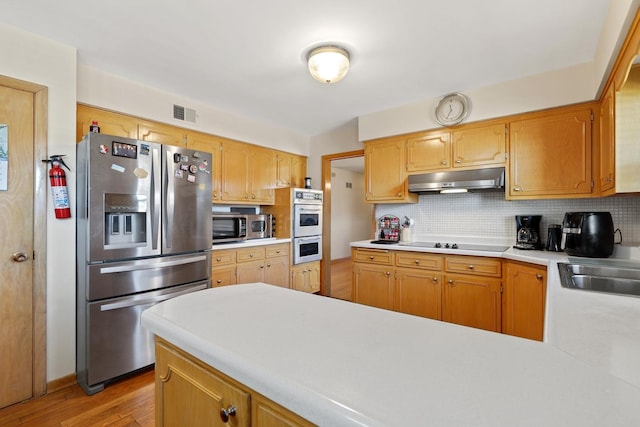 kitchen with sink, light wood-type flooring, kitchen peninsula, stainless steel appliances, and backsplash