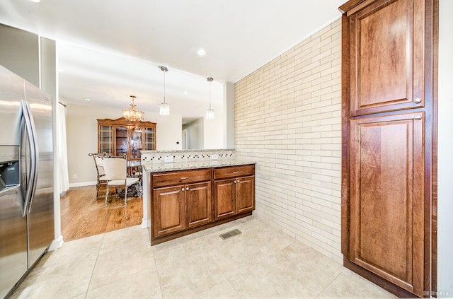 kitchen featuring light stone countertops, pendant lighting, a notable chandelier, stainless steel fridge with ice dispenser, and tasteful backsplash