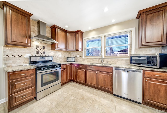 kitchen featuring light stone counters, wall chimney range hood, tasteful backsplash, appliances with stainless steel finishes, and sink