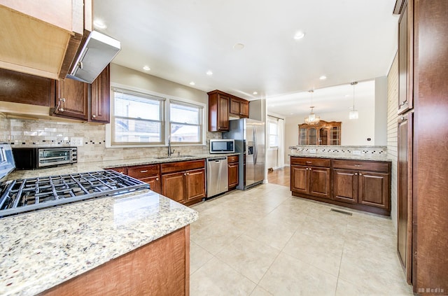 kitchen featuring light stone countertops, decorative light fixtures, stainless steel appliances, tasteful backsplash, and sink