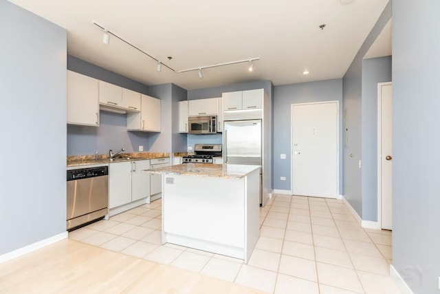 kitchen with stainless steel appliances, sink, white cabinets, light stone counters, and a kitchen island