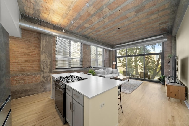 kitchen featuring light hardwood / wood-style flooring, a kitchen bar, gas range, and brick wall