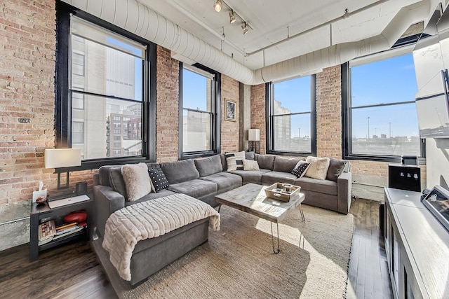 living room featuring brick wall, track lighting, and hardwood / wood-style floors