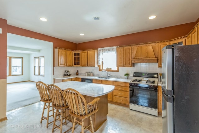 kitchen with custom range hood, brown cabinetry, freestanding refrigerator, a sink, and gas range