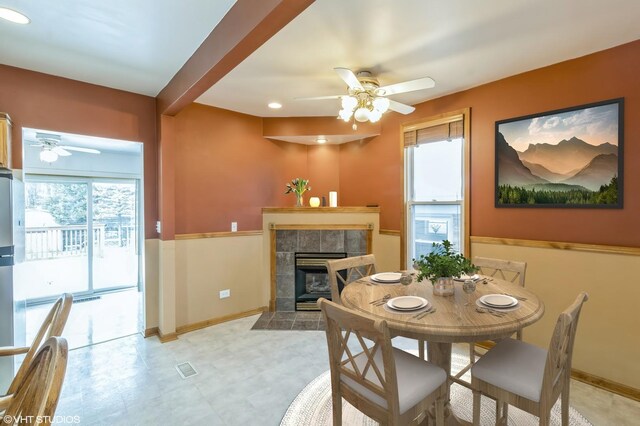 dining space featuring ceiling fan, a wealth of natural light, beam ceiling, and a tiled fireplace