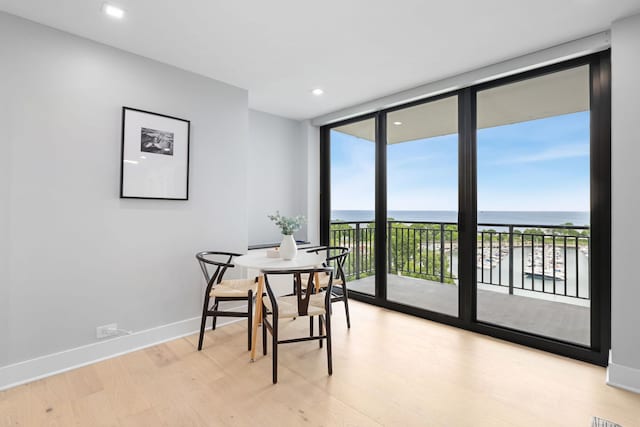 dining space featuring floor to ceiling windows, light wood-type flooring, a wealth of natural light, and a water view