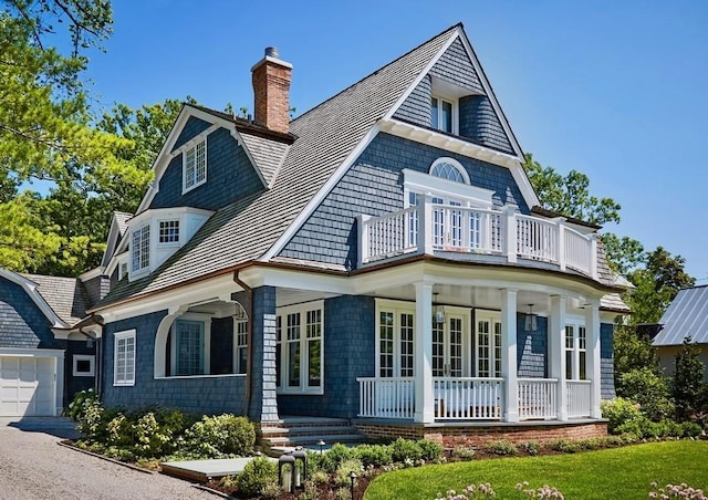 rear view of house featuring a garage, a balcony, and covered porch