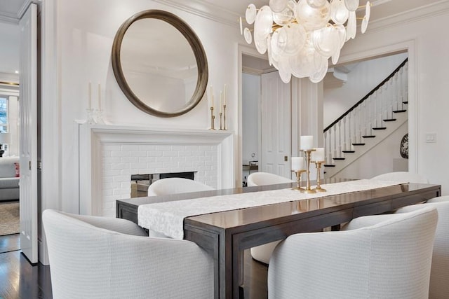 dining area with ornamental molding, a brick fireplace, hardwood / wood-style floors, and a notable chandelier