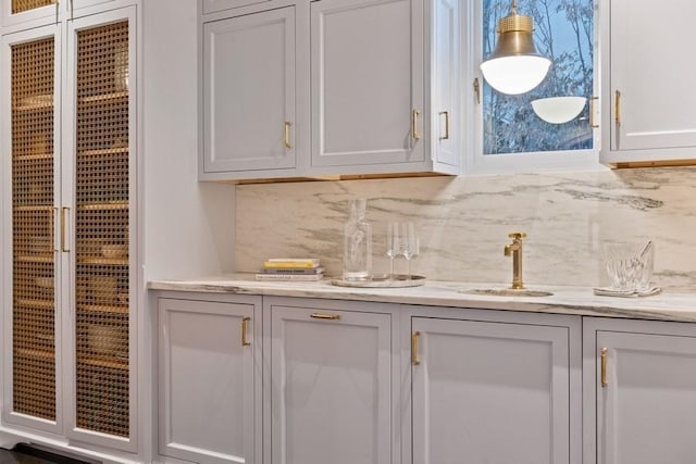 bar with tasteful backsplash, sink, light stone counters, and white cabinets