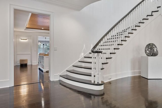 stairs featuring hardwood / wood-style floors, ornamental molding, and a raised ceiling