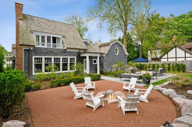 rear view of house with a patio, a balcony, and an outdoor living space with a fire pit