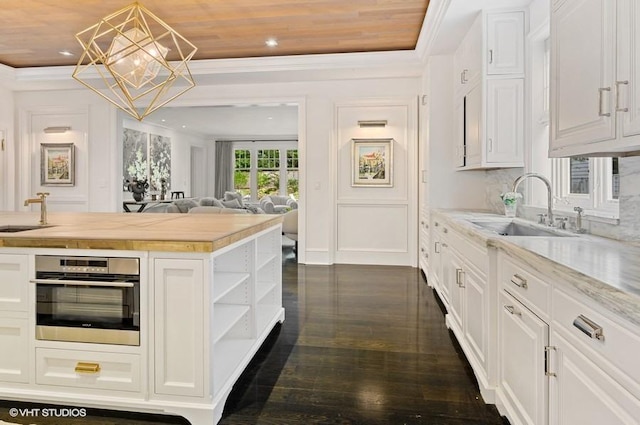 kitchen featuring sink, hanging light fixtures, white cabinets, wood counters, and oven