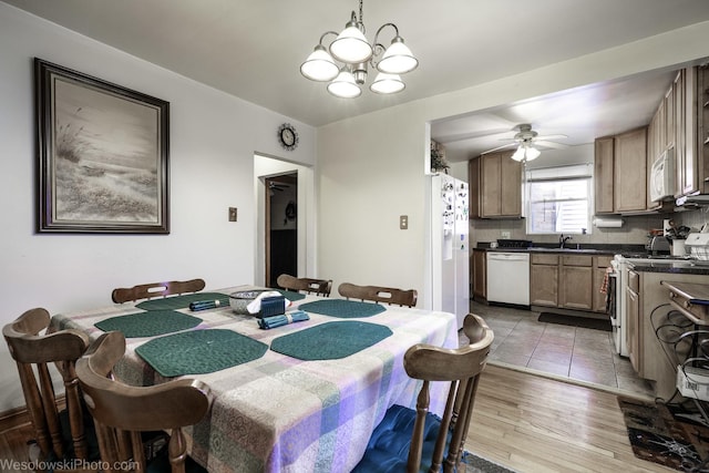 dining space with sink, ceiling fan with notable chandelier, and light hardwood / wood-style flooring