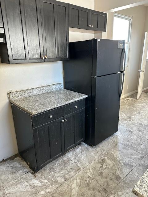 kitchen featuring light stone counters and black refrigerator