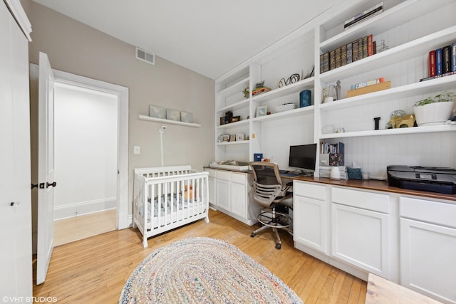 bedroom with light wood-type flooring, built in desk, and a nursery area