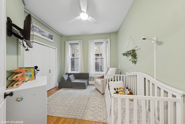 bedroom with ceiling fan, hardwood / wood-style floors, and a crib