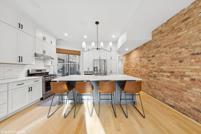 kitchen featuring white cabinets, stainless steel appliances, brick wall, and an island with sink