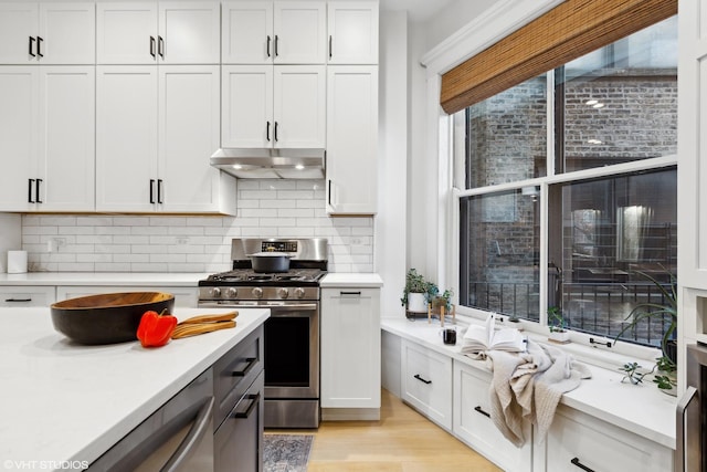 kitchen with stainless steel range with gas stovetop, light hardwood / wood-style flooring, white cabinets, and tasteful backsplash