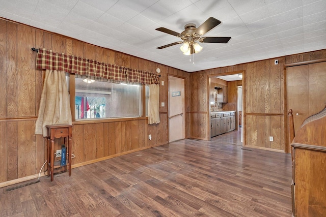 empty room featuring dark hardwood / wood-style floors, ceiling fan, and wooden walls