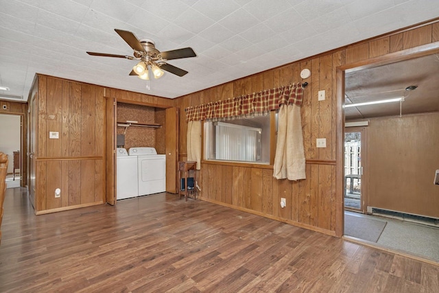 unfurnished living room with wooden walls, wood-type flooring, ceiling fan, baseboard heating, and washing machine and dryer