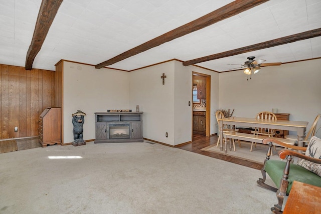 carpeted living room featuring ceiling fan, wooden walls, a fireplace, and beam ceiling