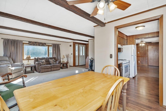 dining area with dark wood-type flooring, ceiling fan, wooden walls, ornamental molding, and beamed ceiling