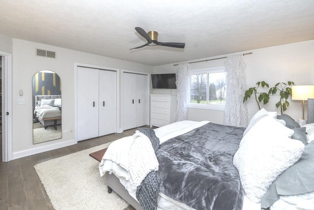 bedroom featuring ceiling fan, dark wood-type flooring, and two closets