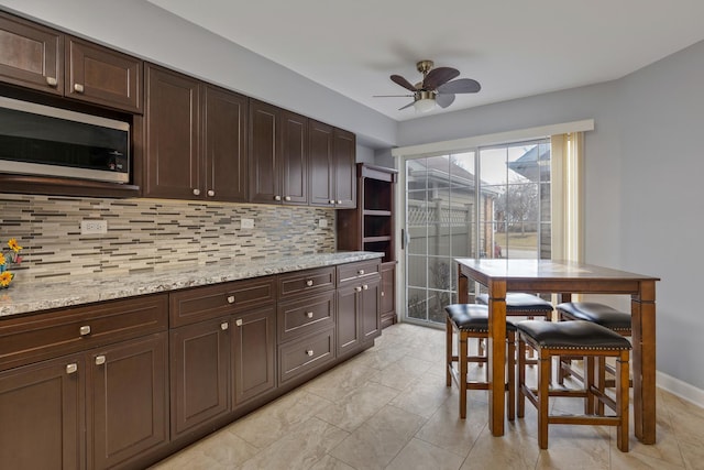 kitchen featuring light stone counters, dark brown cabinetry, decorative backsplash, and ceiling fan