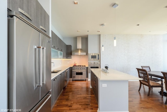 kitchen with wall chimney range hood, hanging light fixtures, dark hardwood / wood-style floors, high end appliances, and a kitchen island