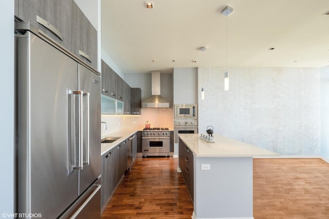 kitchen with wall chimney exhaust hood, wood-type flooring, a center island, hanging light fixtures, and high quality appliances