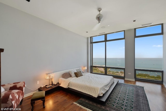 bedroom featuring floor to ceiling windows, a water view, hardwood / wood-style floors, and ceiling fan