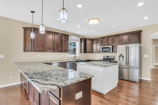 kitchen featuring stainless steel appliances, a kitchen island, hanging light fixtures, and light stone countertops