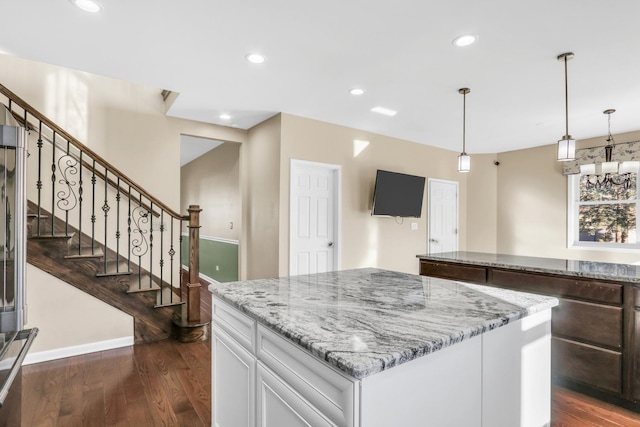 kitchen featuring white cabinets, a center island, light stone counters, hanging light fixtures, and dark hardwood / wood-style floors