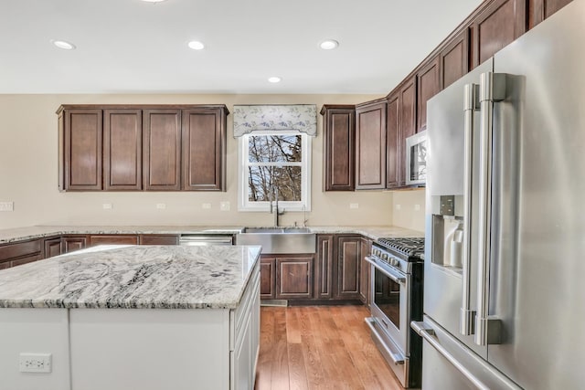 kitchen featuring appliances with stainless steel finishes, light stone countertops, a kitchen island, sink, and light hardwood / wood-style flooring