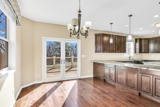 kitchen with light stone countertops, a chandelier, pendant lighting, dark hardwood / wood-style floors, and dark brown cabinetry