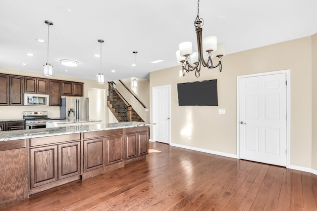 kitchen featuring light stone counters, a chandelier, dark hardwood / wood-style floors, hanging light fixtures, and stainless steel appliances