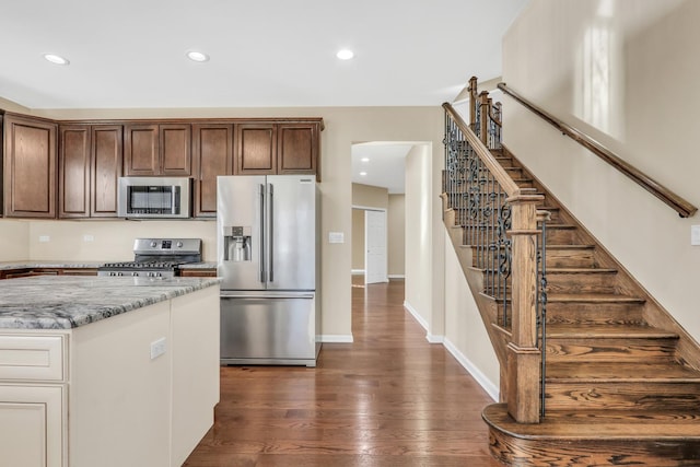 kitchen featuring light stone countertops, appliances with stainless steel finishes, dark brown cabinetry, and dark hardwood / wood-style floors