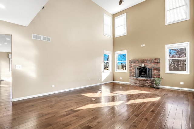 unfurnished living room featuring dark wood-type flooring, high vaulted ceiling, ceiling fan, and a brick fireplace