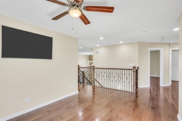 spare room featuring ceiling fan with notable chandelier and hardwood / wood-style floors