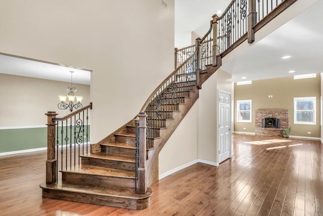 staircase featuring a towering ceiling, a brick fireplace, hardwood / wood-style flooring, and a notable chandelier