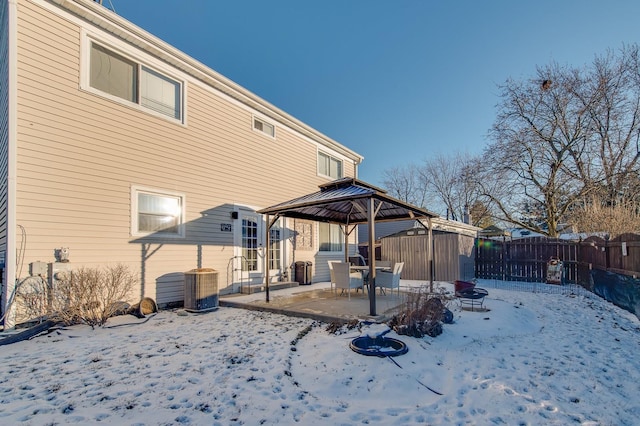 snow covered back of property featuring a storage unit, a fire pit, central air condition unit, and a gazebo