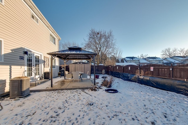 snowy yard with a gazebo, a storage unit, central AC, and a patio