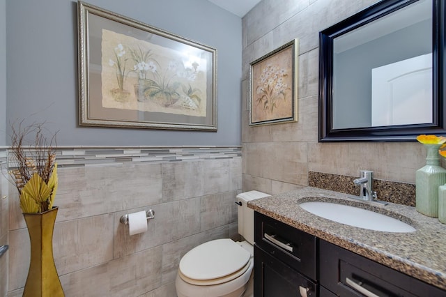 bathroom featuring toilet, vanity, and tile walls