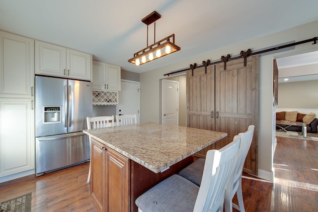 kitchen featuring a barn door, hanging light fixtures, a center island, light stone countertops, and stainless steel fridge