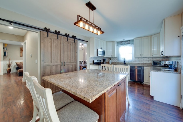 kitchen featuring pendant lighting, a kitchen island, a barn door, white cabinetry, and appliances with stainless steel finishes