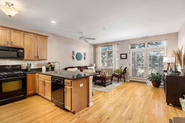 kitchen with black appliances, dark stone counters, light hardwood / wood-style floors, sink, and kitchen peninsula